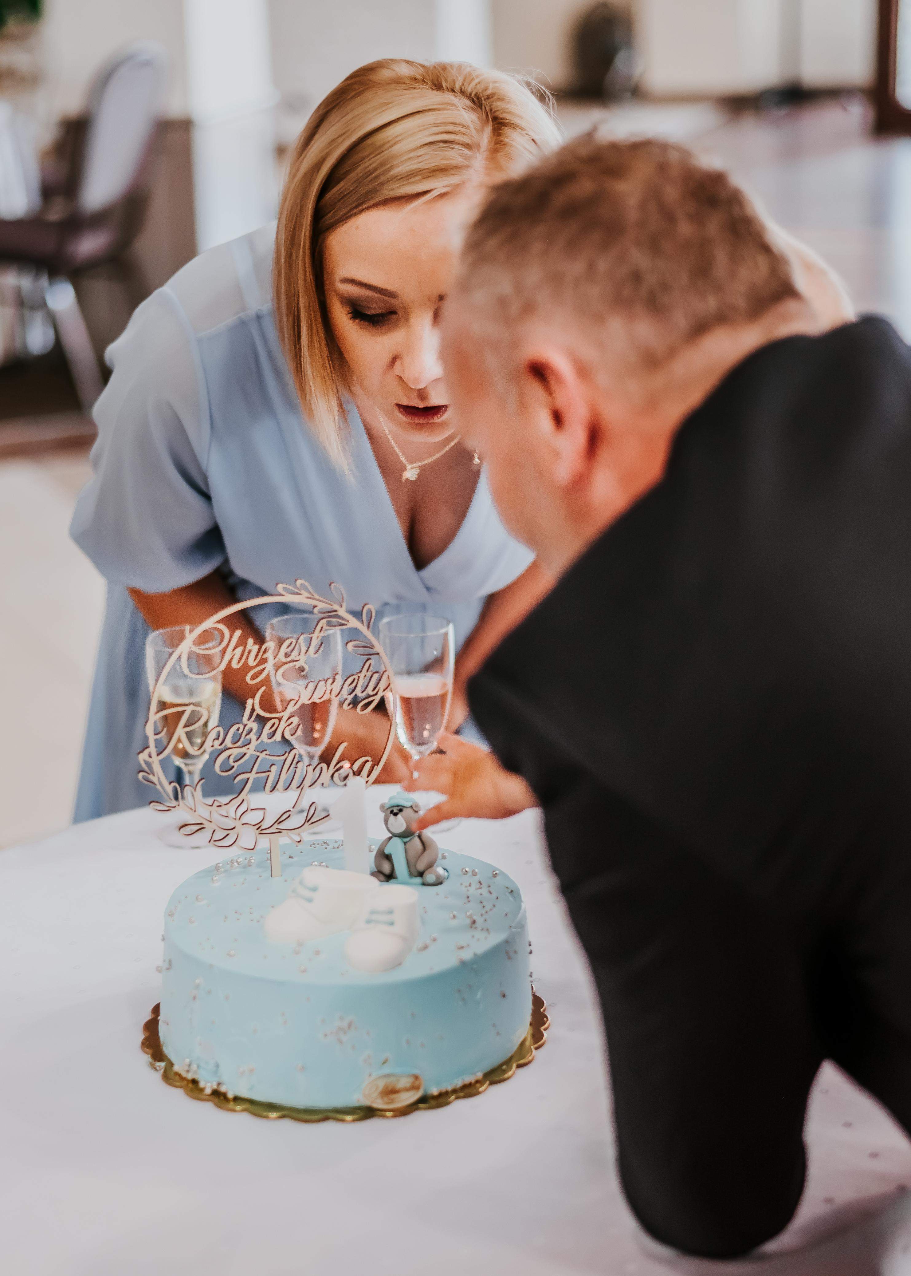 Zdjęcie rodziców, którzy dmuchają świeczki na torcie z okazji chrztu świętego syna